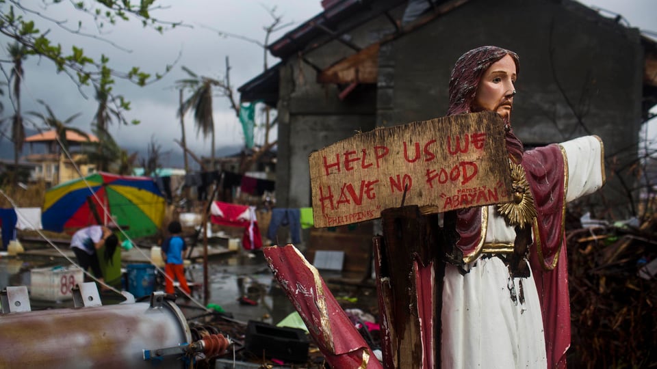 Eine Jesusstatue mit einem Schild, worauf eine Bitte um Hilfe steht.