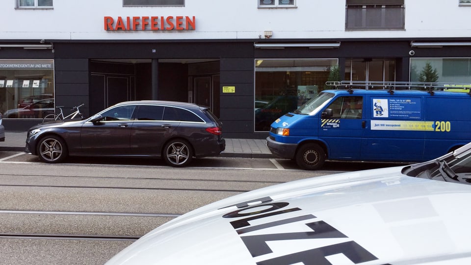Blick auf die Raiffeisenbank von der Strasse. Im Vordergrund ein Schriftzug eines Polizeifahrzeugs