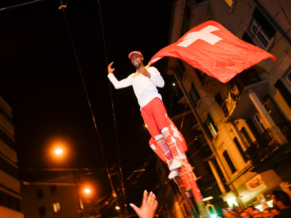 Ein Mann steht auf einer Stange und schwenkt die Schweizerfahne. 