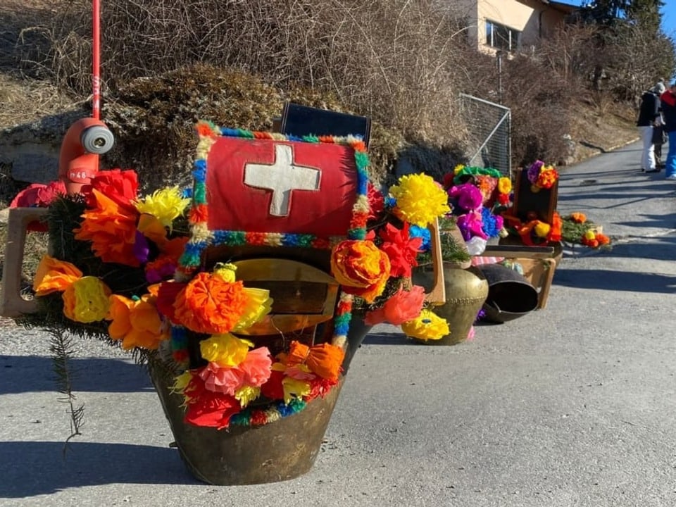 Glocken Grosse, mit farbigen Papierblumen dekorierte Glocken stehen in einer Reihe aufgestellt.