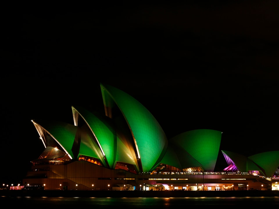 Die Oper von Sydney bei Nacht. Sie ist grün beleuchtet.
