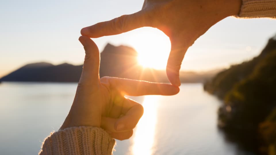 eine Person formt mit den Händen ein Viereck im Sonnenuntergang