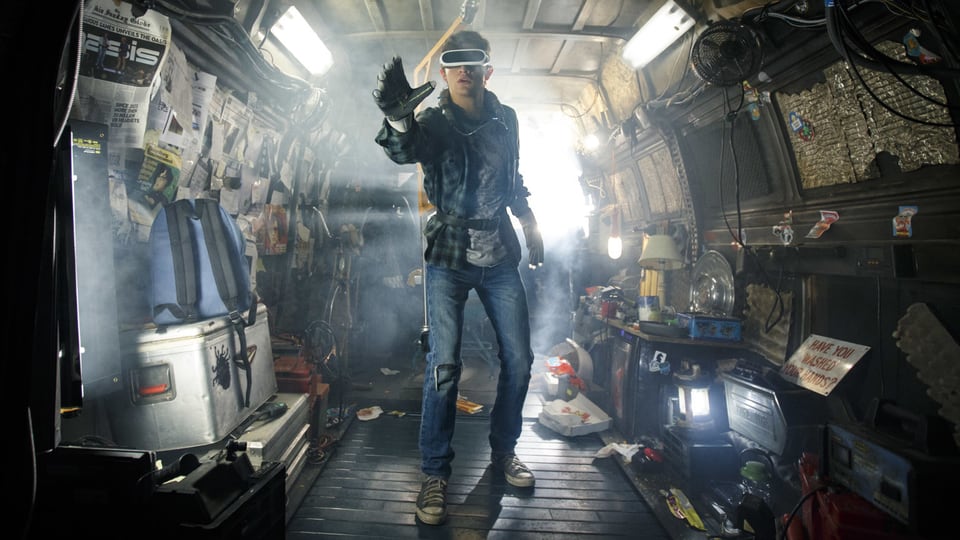 Ein junger Mann mit VR-Brille steht in einem zugemüllten Lieferwagen und streckt die Hand aus.