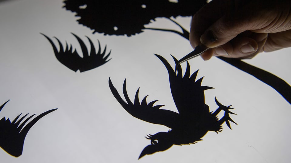 Eine Hand hält einen ausgeschnittenen Vogel mit einer Pinzette fest.
