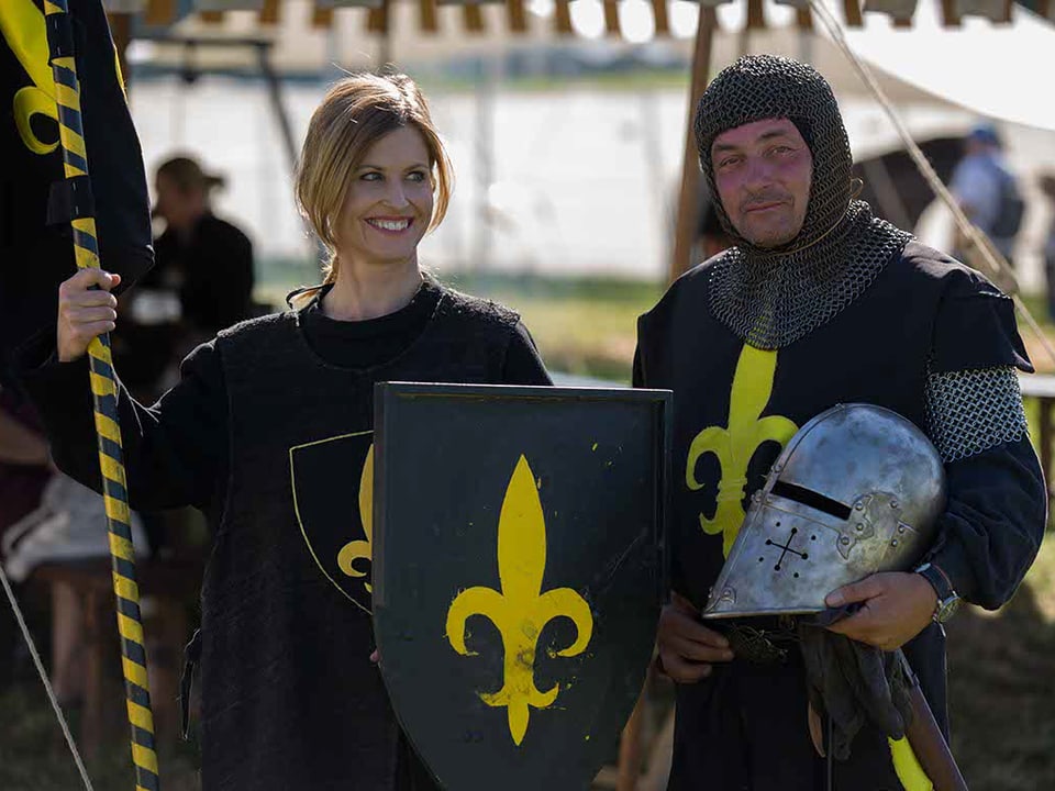Ritter und Knappe nebeneinander in mittelalterlicher Kleidung mit Wappen, Schild und Banner.