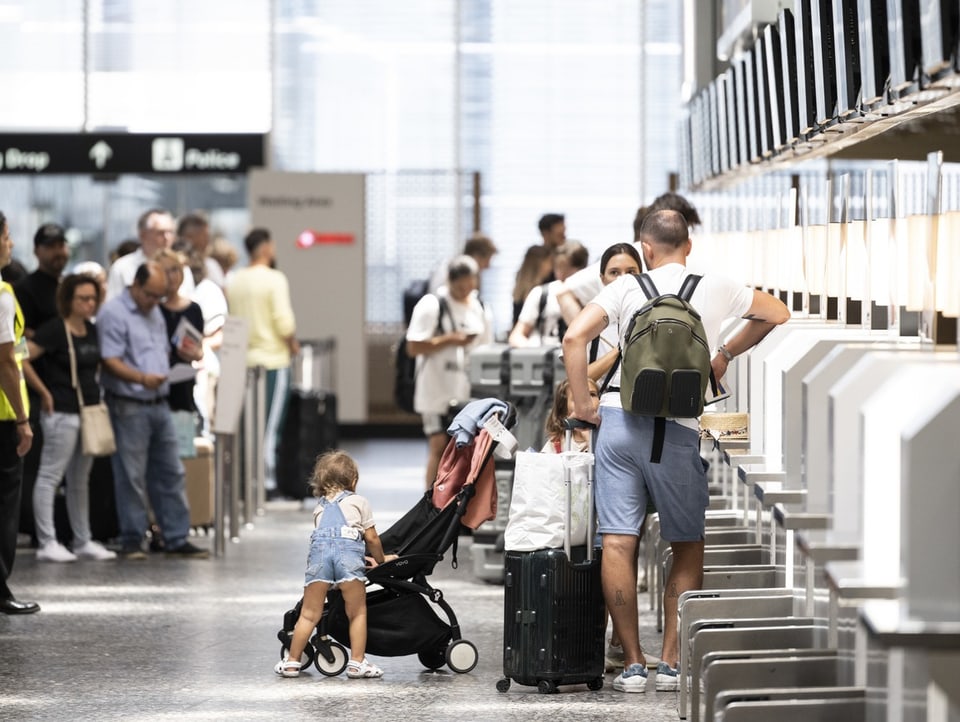 Eine Familie mit zwei Kindern und Kinderwagen steht an einer Reihe von Check-In-Schalter in einem Flughafen.