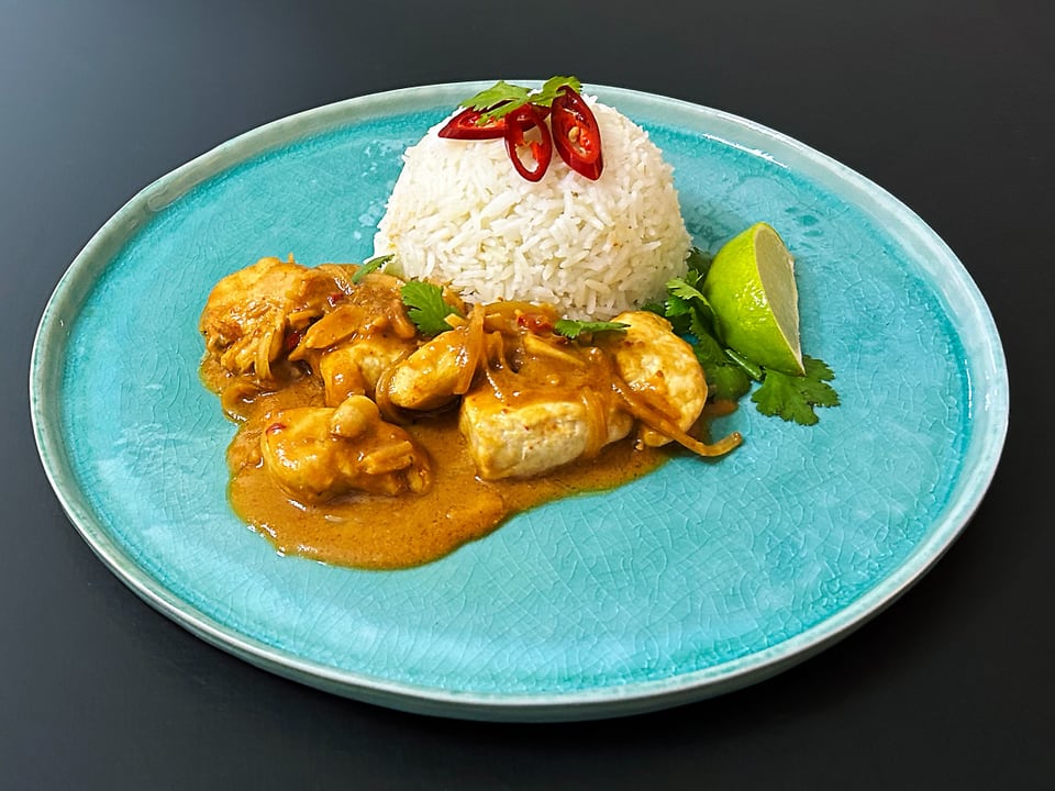 Teller mit Curry-Hühnchen, Reis, Limettenspalte und Chili auf blauem Teller