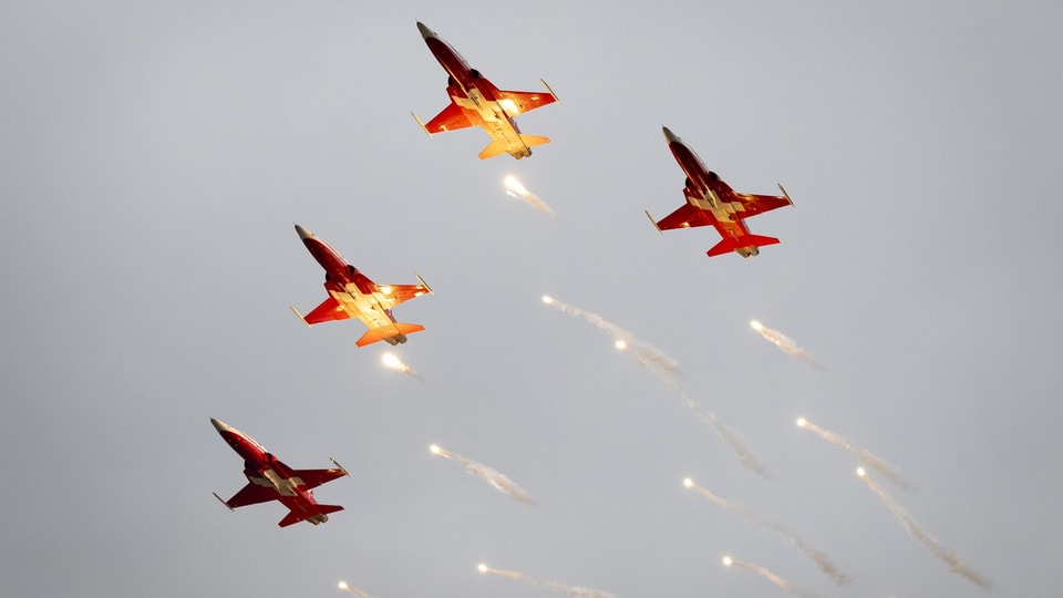 Vier Kunstflugstaffeln fliegen durch den Himmel und werfen Feuerwerkskörper ab.