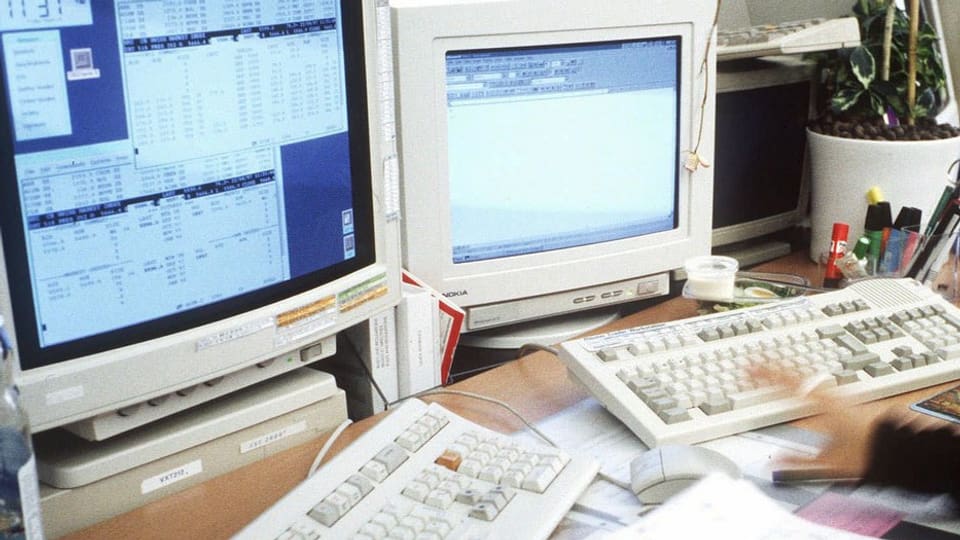 Zwei Bildschirme mit Kursdaten und zwei Tastaturen mit einer Hand an einem Handelsarbeitsplatz einer Bank