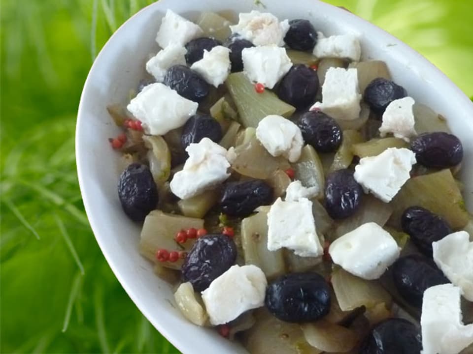 Fenchel-Zwiebel-Gemüse auf einer weissen Schale angerichtet und mit Feta und Oliven garniert.