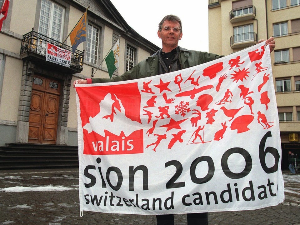 Ein Mann hält eine Fahne mit dem Logo der Olympiakandidatur Sion 2006.