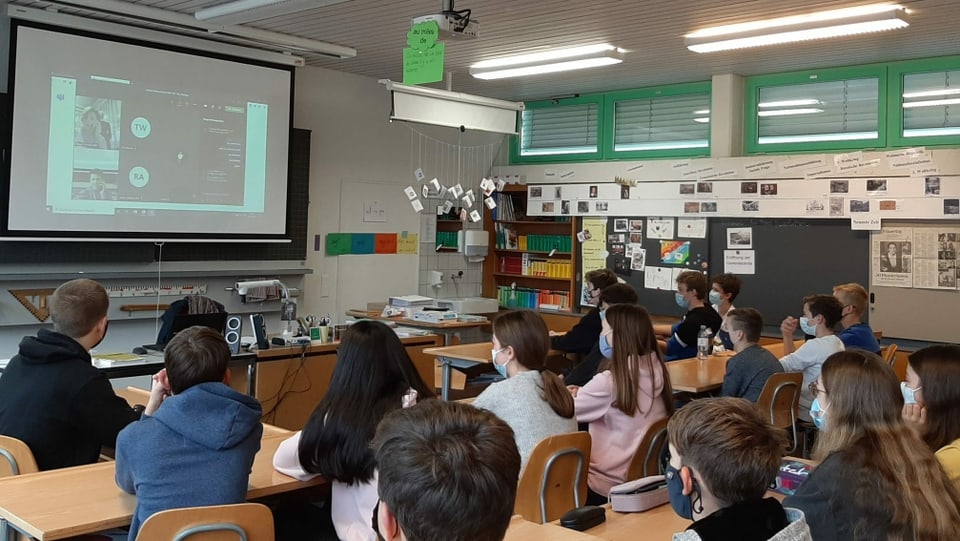 Der Rest der Klasse verfolgt das Gespräch auf einer Leinwand.