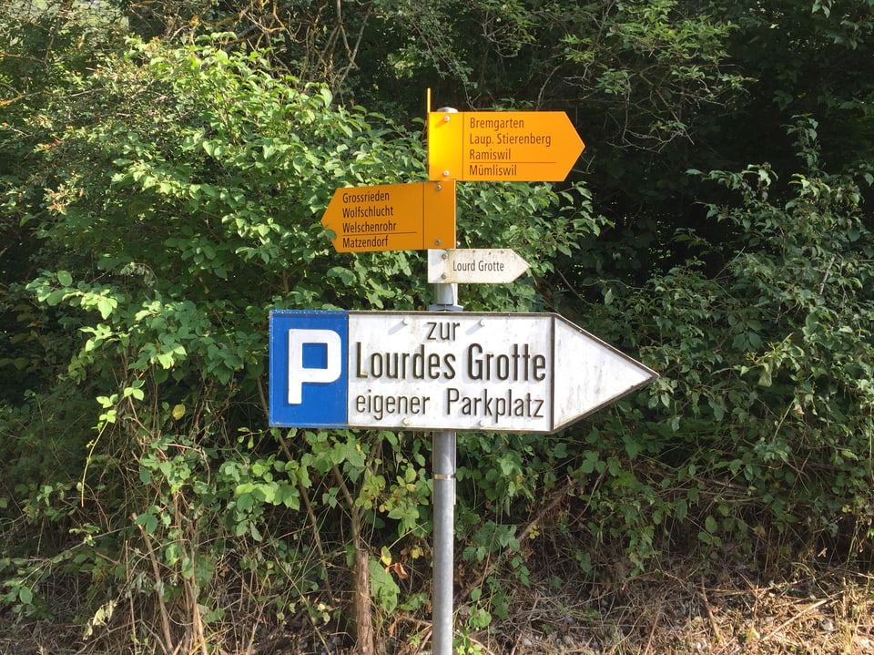 Wanderwegweiser, darunter ein Schild "Parkplatz zur Lourdes Grotte"