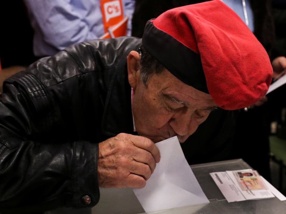 Mann mit roter Kappe küsst Wahlzettel, bevor er ihn in die Urne wirft.