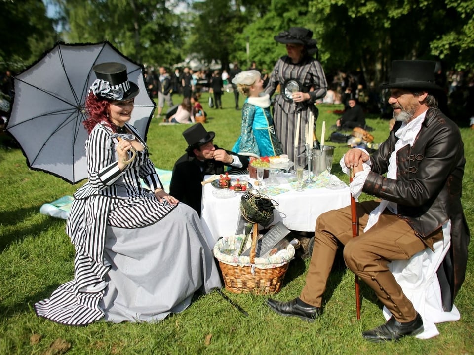 Menschen in viktorianischen Kleidern machen im Park ein Picknick. 
