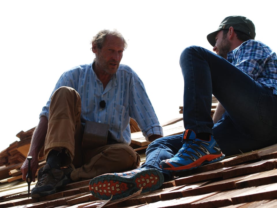 Nik Hartmann sitzt mit Schindelbauer auf einem Dach, welches eingedeckt wird. 