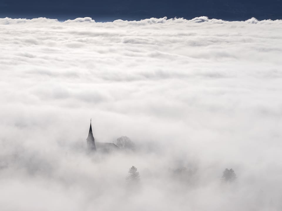 Die Spitze des Kirchturmes ragt gerade noch aus der Nebeldecke heraus.