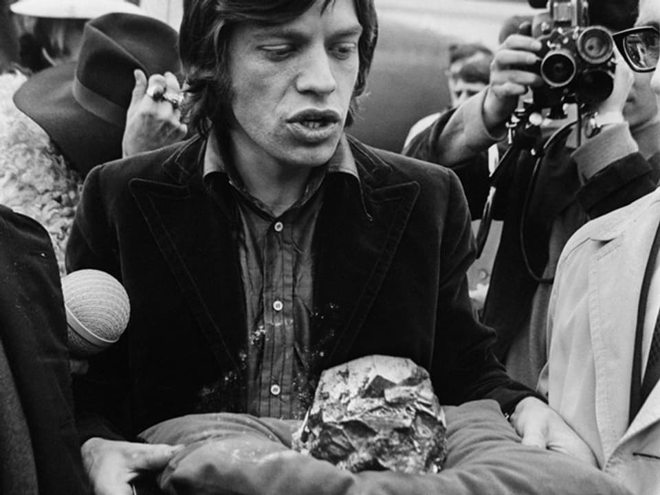 Mick Jagger wird 1967 bei seiner Ankunft am Flughafen einen Stein überreicht