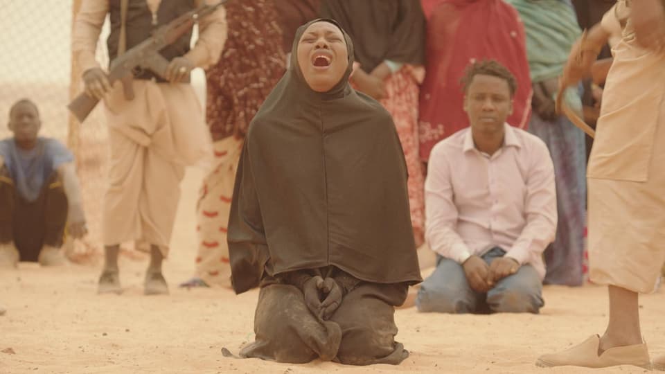 Eine Frau in schwaruem Gewand und Kopftuch kniet schreiend im Sand.