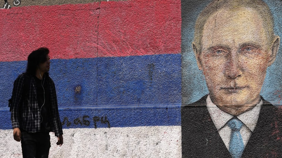 Serbische Flagge neben Wandmalerei von Putin