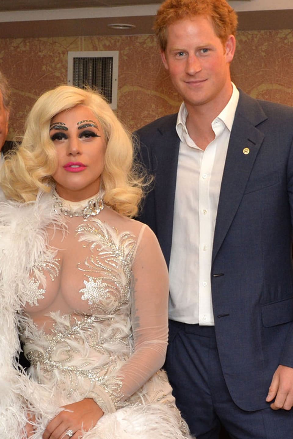 Lady Gaga in einem weissen, transparenten Kleid posiert mit Prinz Harry, der einen blauen Anzug trägt.