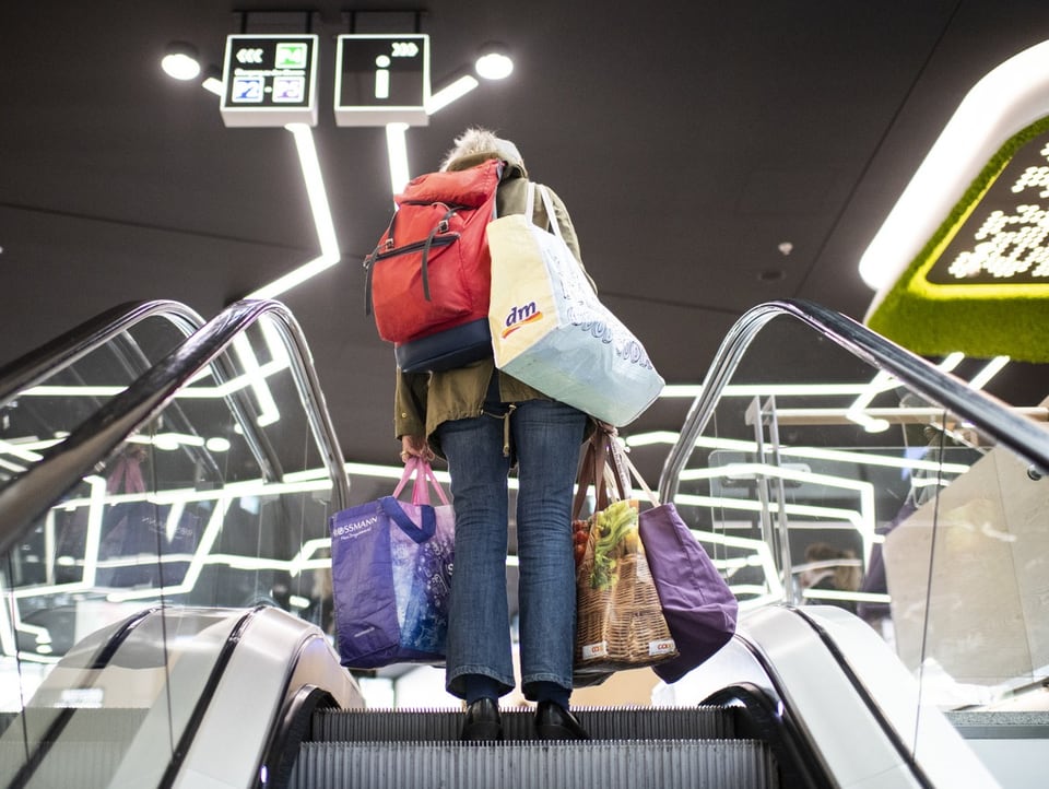 Eine Person mit mehren Einkaufstaschen fährt eine Rolltreppe hoch.