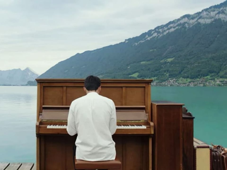 Mann in weissem Hemd spielt auf einem Piano am See