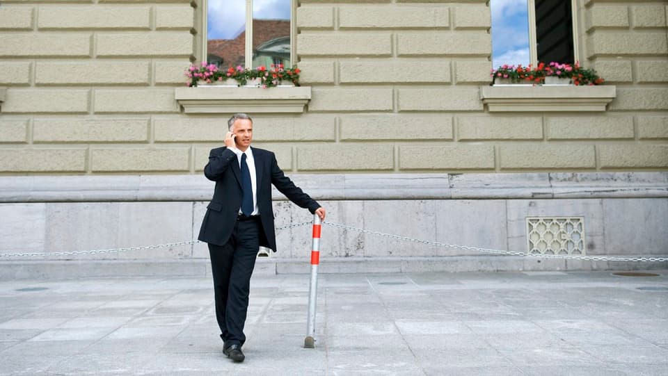 Didier Burkhalter, vor der Bundeshausfassade mit Handy am Ohr, stützt sich auf einen Poller.