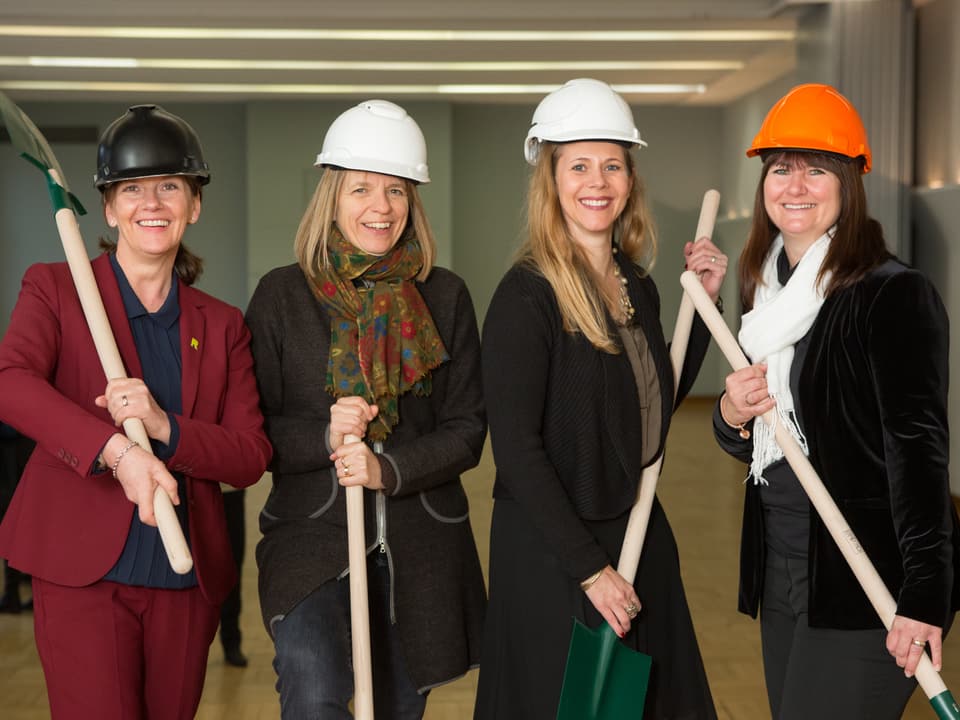 Die vier Frauen, welche das Projekt verantworten, posieren mit Helmen und Schaufeln im Lukas-Saal. 