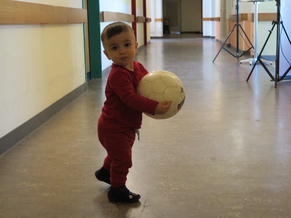 Kleiner Junge steht mit Fussball in der Hand im Gang