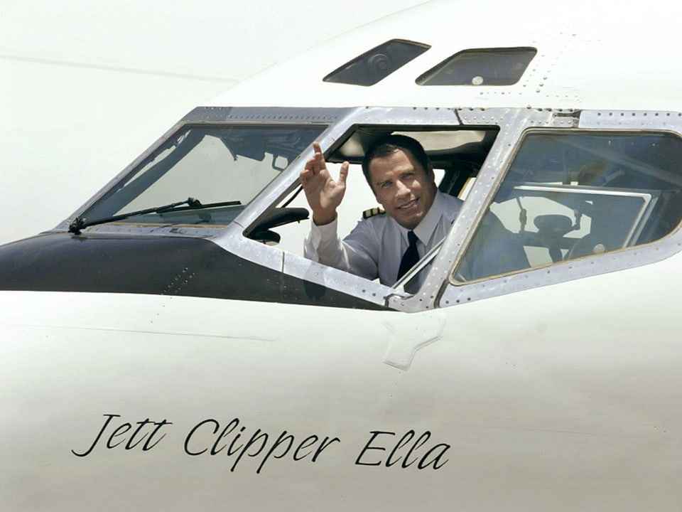John Travolta winkt aus Flugzeug-Cockpit.