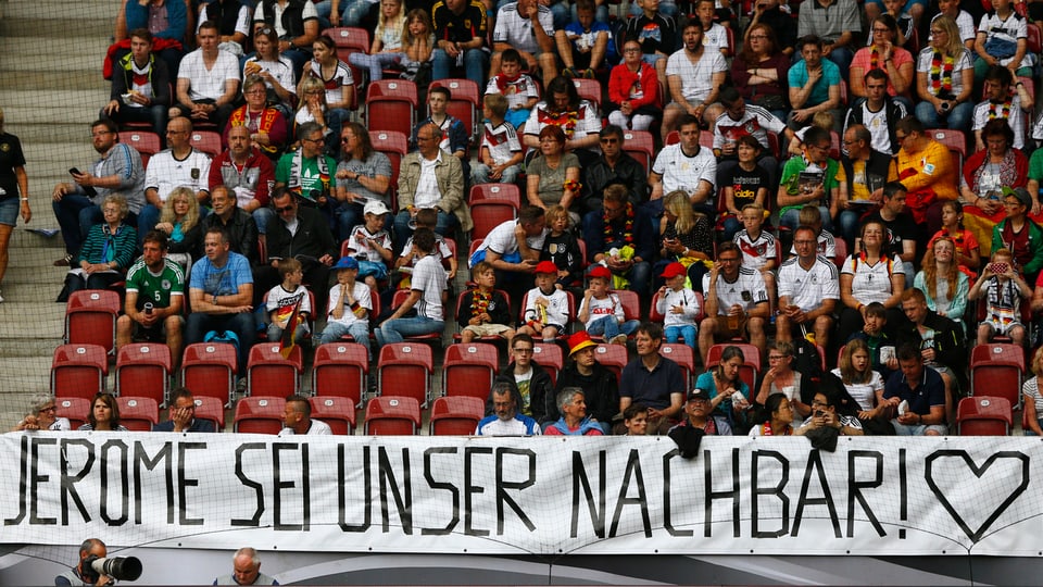 Fans in Stadionsitzreihen, darunter grosses Plakat mit Aufschrift «Jérôme sei unser Nachbar»