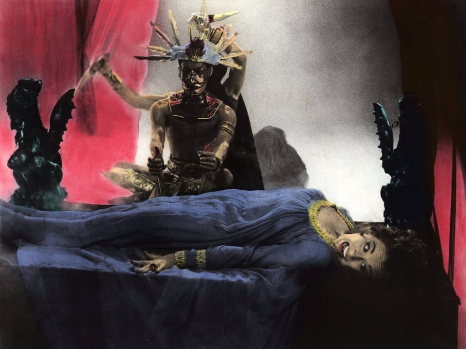Szenische Darstellung mit Dämon und langer Figur in blaue Robe gekleidet, dramatisch beleuchtet.