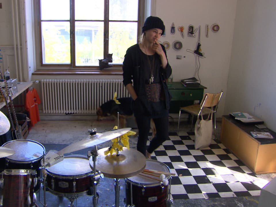 Anja Rüegsegger in ihrem Atelier: im Vordergrund ein Schlagzeug, hinter ihr Werkzeug und ihr Hund.