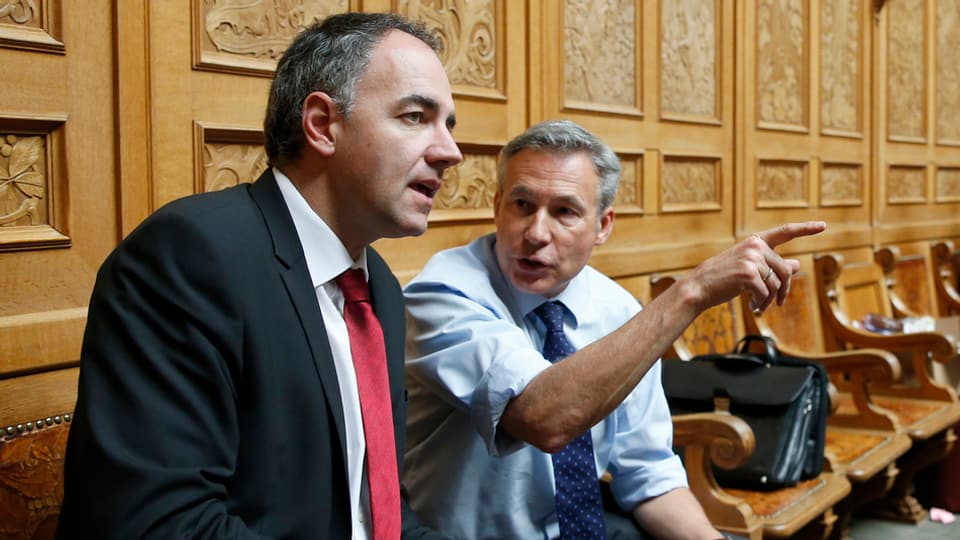 Christophe Darbellay und Adrian Amstutz sitzen Schulter an Schulter hinten im Nationalratssaal.