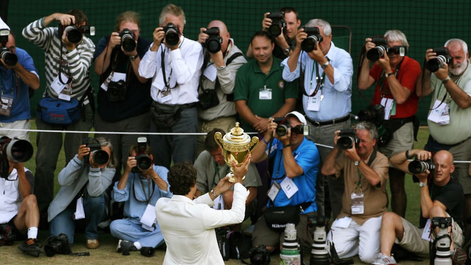 Rückenansicht von Federer, wie er den Fotografen den Pokal entgegenstemmt.