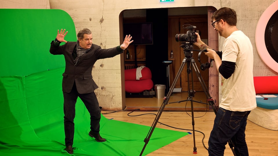 Boris Blank steht auf einem grünen Stück Stoff vor einer grünen Wand und blickt in eine Kamera.