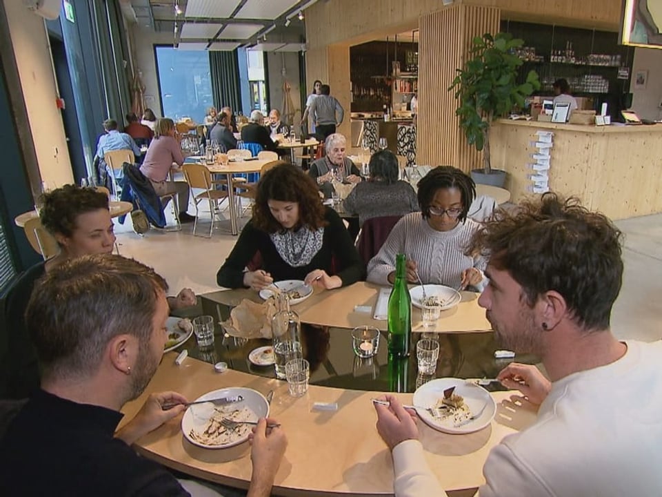 Gäste sitzen um einen Tisch und essen. 