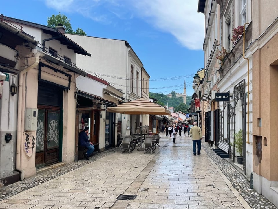 Blick auf eine Gasse in Bascarsija in Sarajevo mit Geschäften und Menschen.