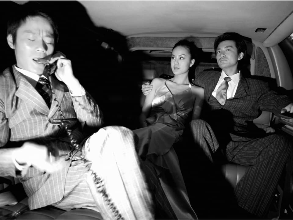 Im Inneren einer Limousine: Im Vordergrund telefoniert ein Mann, hinten sitzt ein junges Paar