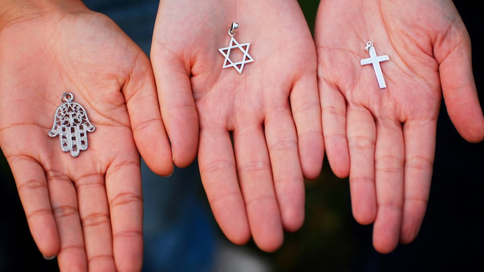 Hände halten Symbole für Islam, Judentum und Christentum in den Händen.