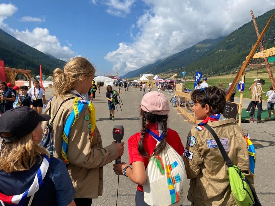 vier Kinder von hinten in Pfadiuniform mit einem Mikrofon