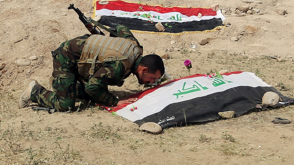 Soldat kniet an einer Leiche, die von einer Fahne bedeckt ist.