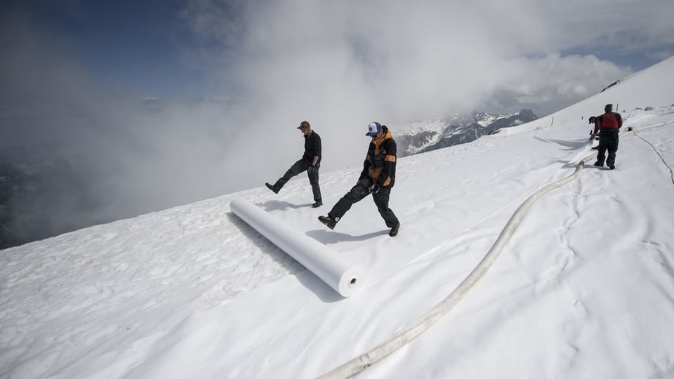 Zwei Männer breiten eine weisse Plane über Schnee aus.
