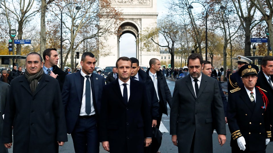 Macron und weitere Männer auf den Champs Elysées, im Hintergrund der Arc de Triopmphe.