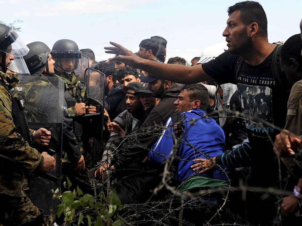 Polizisten und Flüchtlinge stehen sich gegenüber, getrennt durch einen Stacheldraht 