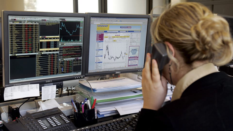 Bildschirm mit Börsenkursen und telefonierende Frau im Vordergrund