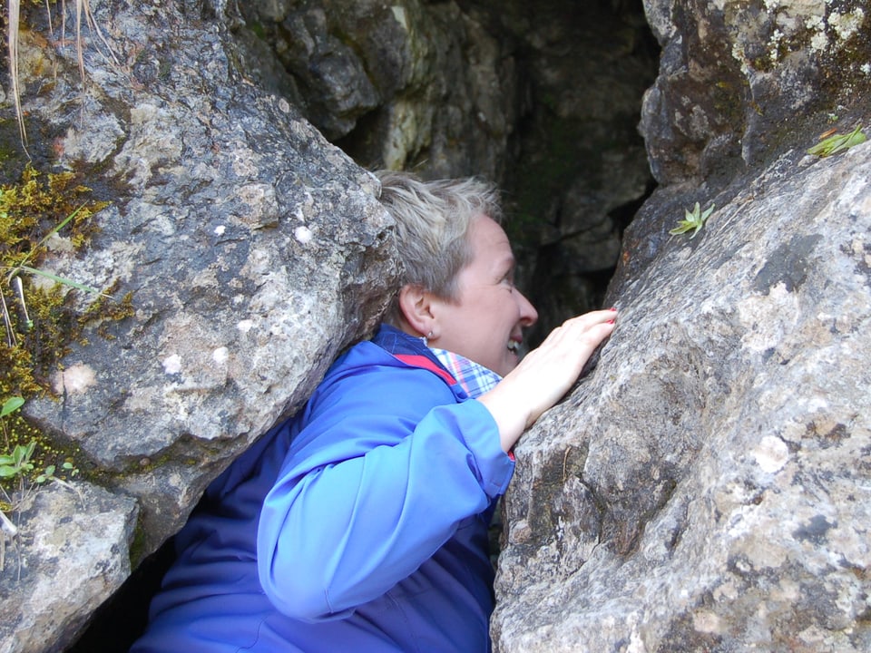 Eine Frau mit blauer Regenjacke in einer Felsspalte.