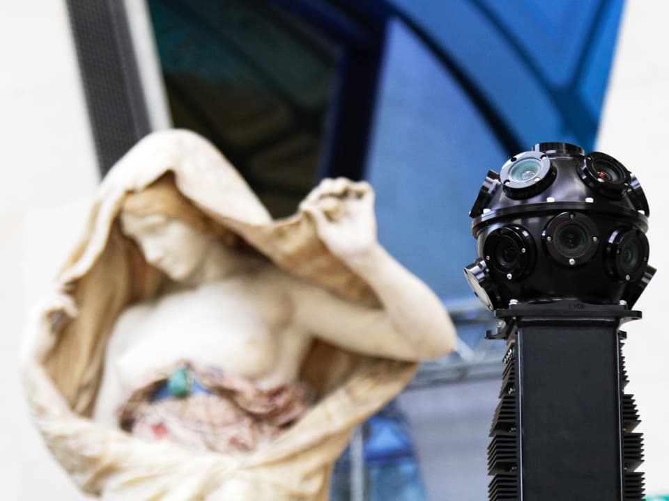 Eine moderne Kamera neben einer alten Statue in einem Museum.