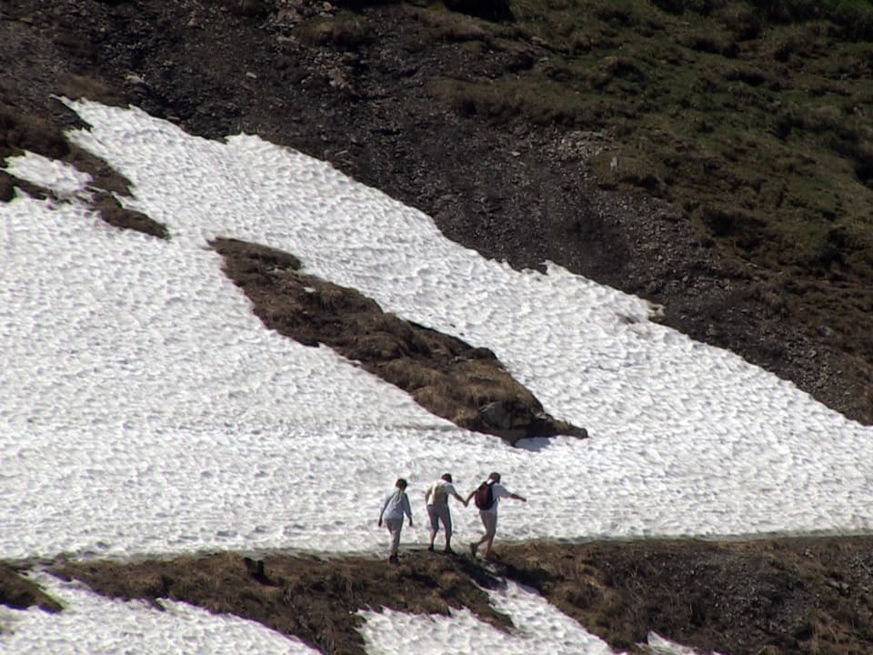Drei Wanderer etwas unsicher zwischen Schneeflecken.